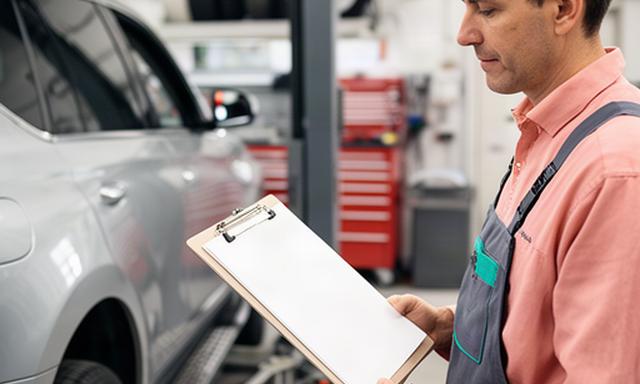 Mechanic reviewing a service document beside a vehicle in a Winnipeg automotive workshop