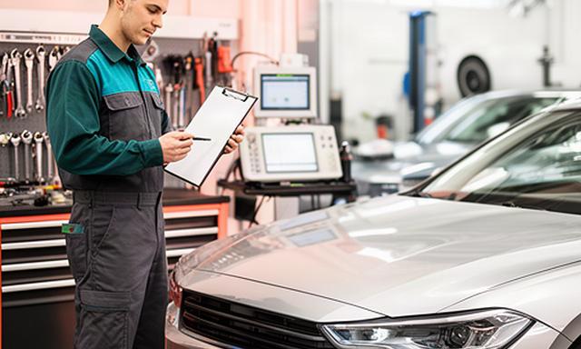 Service advisor reviewing a vehicle inspection beside a car in a Winnipeg automotive workshop