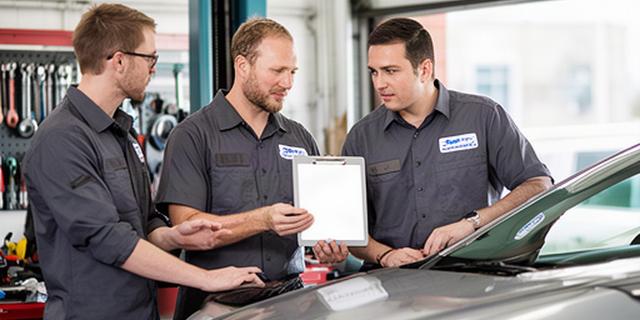 Automotive repair team reviewing a vehicle inspection beside a service bay